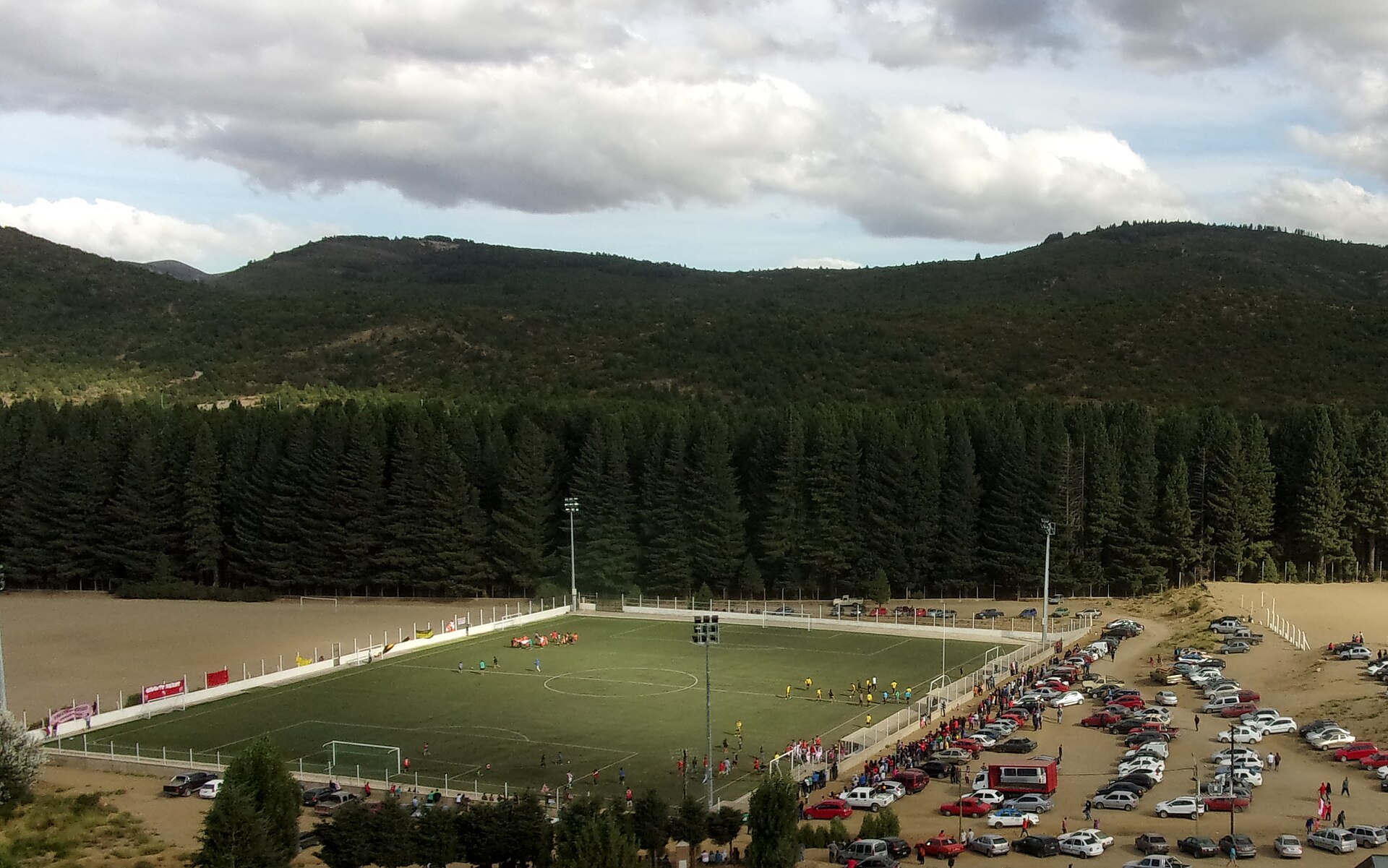 Partido de fútbol de noche en una cancha de césped sintético con iluminación